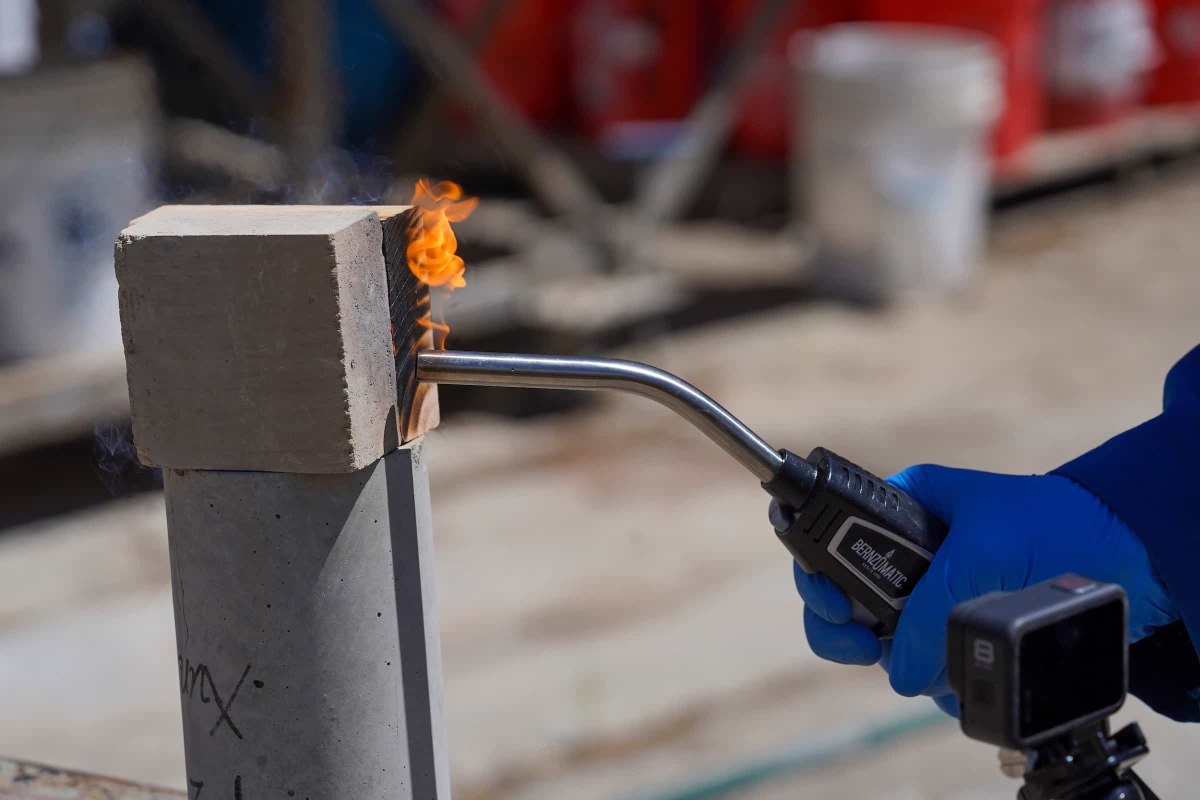 A blow torch of 3,400 degrees Fahrenheit blasts a block of wood and an earth block at the same time.