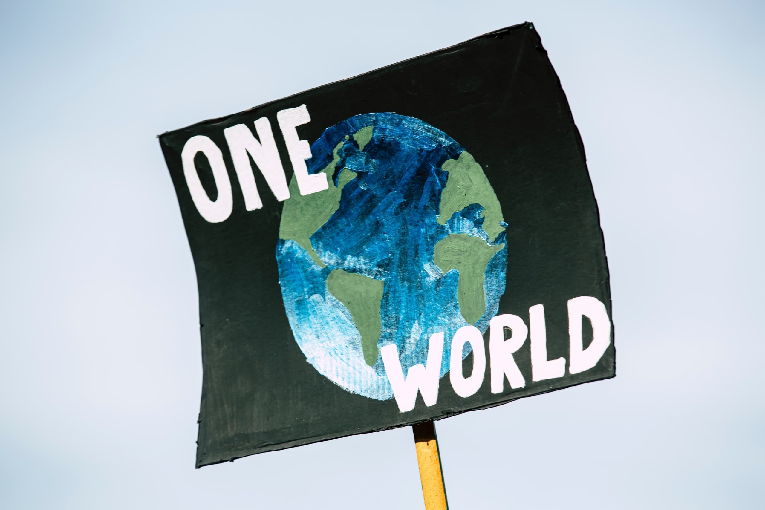 A sign with the words "One World" against an illustration of the Earth against a black background.