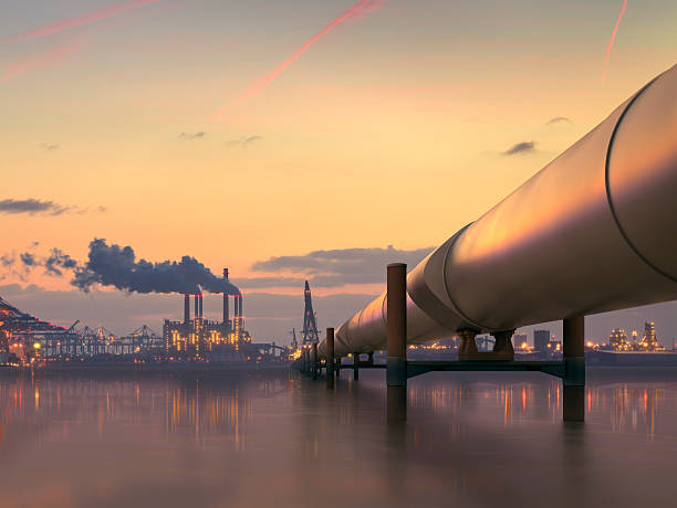 An ocean oil pipeline. In the background, smoke rises from an industrial factory.