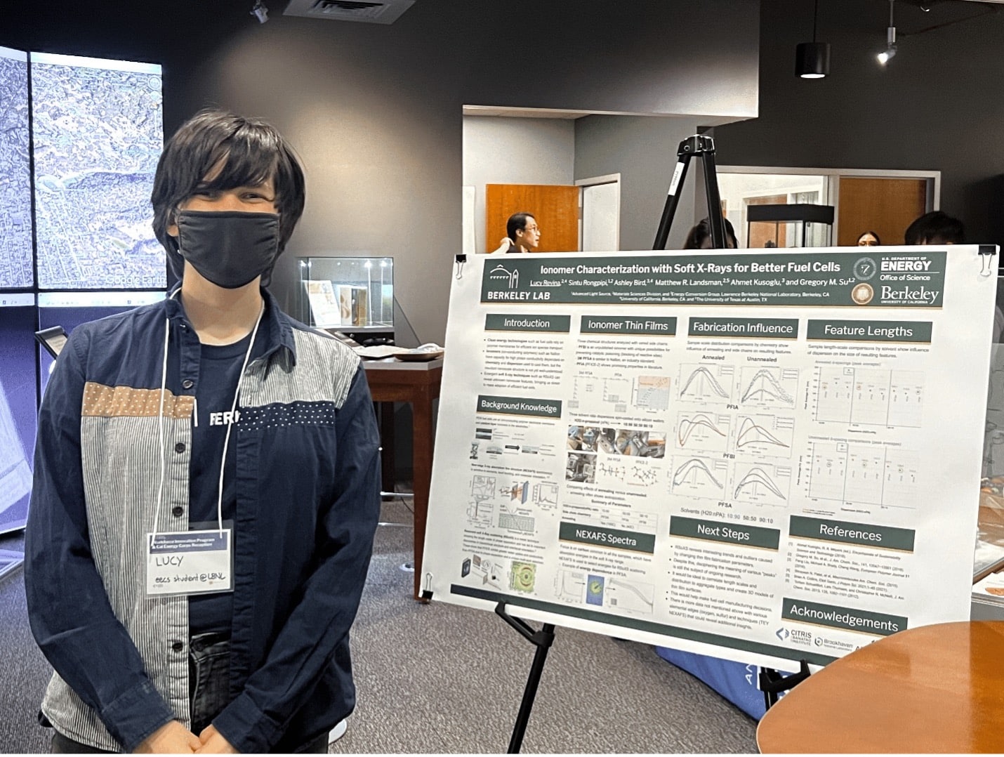 A student with short black hair and a black face mask poses next to a research poster at a poster session inside the CITRIS Tech Museum at UC Berkeley.