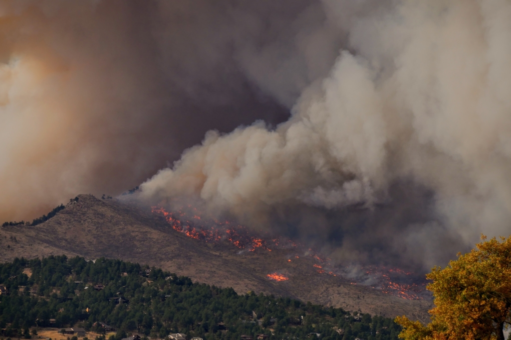 A wildfire charges up a mountain slope, producing a thick haze of smoke